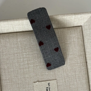 Detail view of gray denim fabric hair clip with red flocked heart patterns on a soft tray