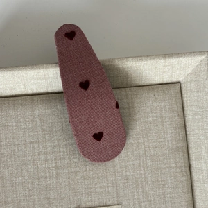 Detail view of purple fabric hair clip with three red flocked heart patterns on a beige tray