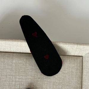 Detail of a black fabric snap hair clip featuring a sweet red embroidered heart pattern