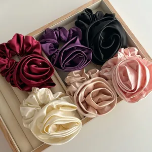 Elegant satin rose flower hair scrunchies in six luxury colors on a wooden tray