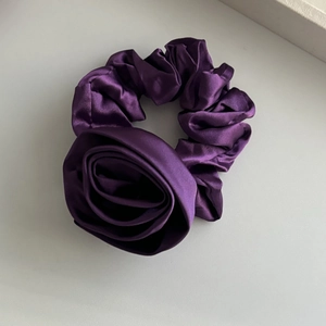 Detailed shot of dark purple satin scrunchie with a large handmade fabric rose accessory