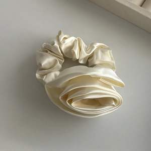 Detailed shot of ivory satin flower hair scrunchie with smooth silk texture and folds