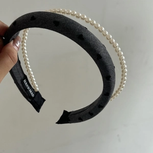 Detailed macro of a grey knitted headband with heart patterns and pearl bead trim