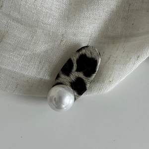 Barrette léopard chic avec grande perle sur un fond minimaliste en tissu beige clair