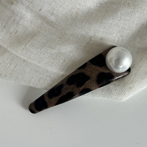 Gros plan d'une pince à cheveux léopard avec perle élégante sur texture lin beige