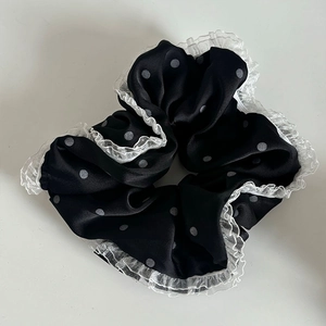 Detailed close-up of a black satin scrunchie with grey polka dots and white lace edges