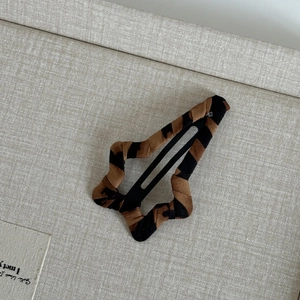 Detail of leopard print fabric star hair clip on a minimalist grey textured background