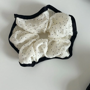 Detailed close-up of white lace fabric hair scrunchie with black polka dots and satin trim