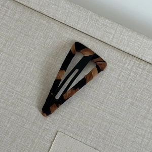 Detail shot of leopard print fabric covered black metal BB hair clip on a beige background