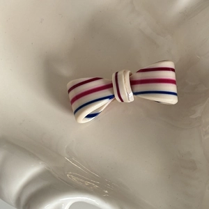 Striped acetate bow hair clip in cream with pink and blue lines on ceramic plate