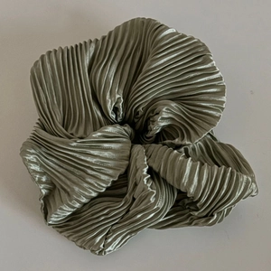 Détail d'un chouchou vert sauge en tissu plissé avec un effet de brillance métallique