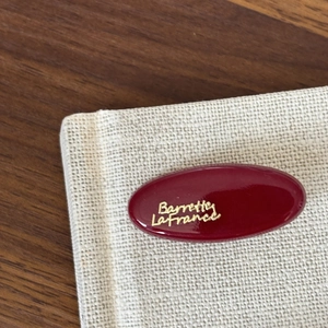 Close-up of a burgundy oval French hair clip with gold lettering on a beige linen fabric