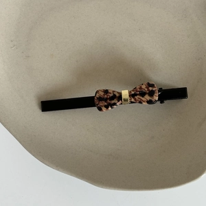 Leopard print bow hair clip with gold buckle on white ceramic plate, minimalist fashion accessory