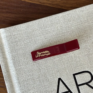 French vintage wine red resin hair clip with gold lettering on a beige fabric background