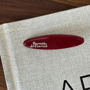 Detailed macro view of a glossy burgundy oval hair clip with gold French text engraving