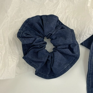 Détail d'un chouchou en jean bleu avec surpiqûres blanches sur papier texturé blanc