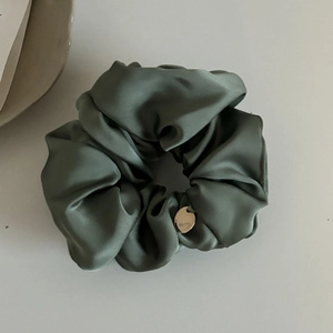 Détail d'un chouchou en satin vert sauge avec plis élégants et breloque dorée