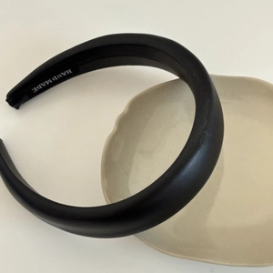 Detail of handmade padded black leather headband with logo label on a ceramic tray