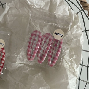 Close-up of three pink and white plaid waterdrop BB clips in branded transparent packaging