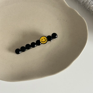 Détail d'une pince à cheveux argentée avec perles facettées noires et breloque smiley
