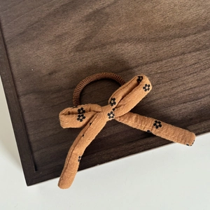 Elastico per capelli con fiocco a fiori marrone in lino su un vassoio di legno