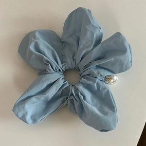 Gros plan détaillé sur un chouchou fleur en tissu bleu clair avec détail perle blanche