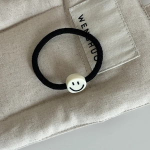 Élastique à cheveux noir minimaliste avec breloque smiley blanc sur fond en toile