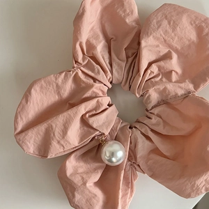 Vue macro détaillée d'un grand chouchou en tissu rose poudré orné d'une perle blanche