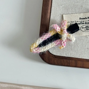 Pink and yellow tweed bow hair clip with metal duckbill base on a linen display