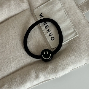 Gros plan d'un élastique à cheveux noir avec une perle minimaliste à motif smiley