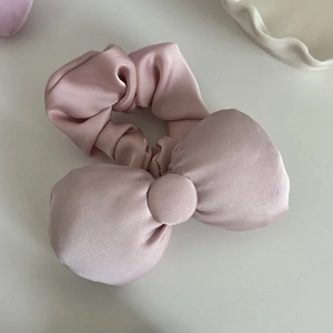 Elegant dusty pink satin scrunchie with a large bow detail on a white surface
