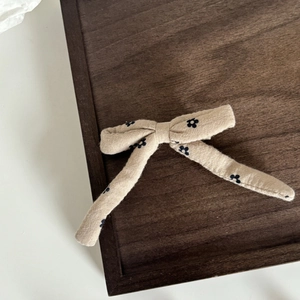 Dettaglio di fermaglio beige con motivo floreale e nastri su vassoio di legno