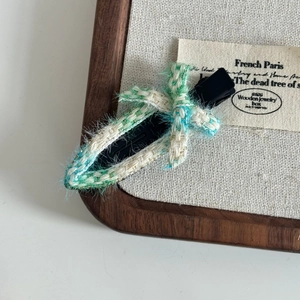 Detailed view of woven tweed duckbill hair clip with fringe bow and textured fabric finish