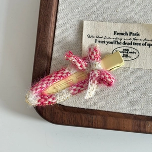 Detail of pink tweed bow hair clip with gold thread fringe on a yellow duckbill clip