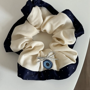 Detail view of navy polka dot and beige fabric hair tie with silver bow and blue button