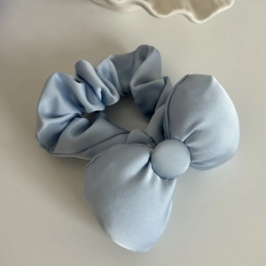 Detailed close-up of light blue satin scrunchie with large bow on a minimalist white surface