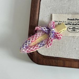 Detail of pink and purple woven hair clip with mini bow on a rustic linen background