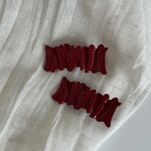 Set of two burgundy red wave-textured hair clips with a glossy finish on white fabric