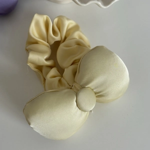 Detail of a creamy yellow satin scrunchie with a large bow showing silky fabric texture