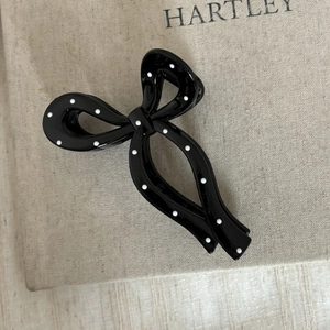 Vue détaillée d'une pince à cheveux noire brillante à pois blancs sur lin beige