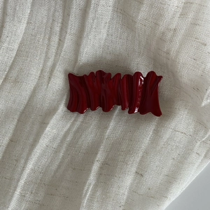 Elegant wavy burgundy red hair clip with a high-gloss finish on a white fabric background