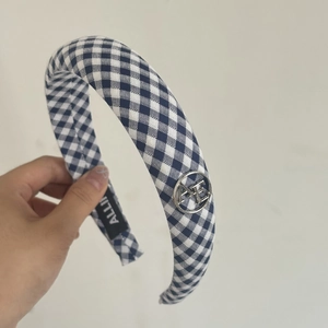 Detailed close-up of blue gingham fabric headband with silver metallic logo ornament