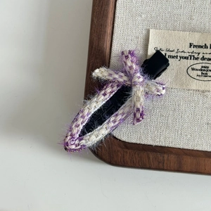 Detail of a purple tweed duckbill hair clip with a bow on a wooden display stand