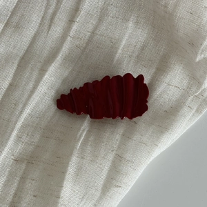 Detailed macro view of dark red hair clip featuring irregular wavy textured resin finish