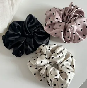 Detailed view of satin heart scrunchies in black, pink and cream white colors