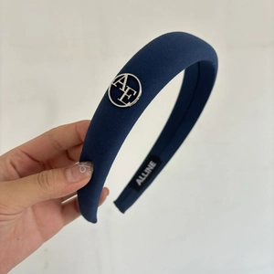 Detail view of navy blue padded headband with silver AE metal charm and inner brand tag
