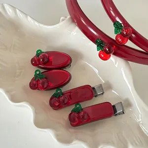 Detail view of red cherry hair clips and headbands set on a white textured ceramic tray