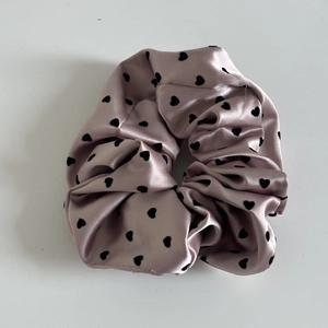 Close-up of pink satin scrunchie with black heart pattern and glossy pleated texture