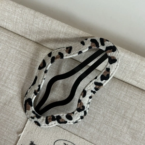 Close-up detail of leopard print fabric hair clip with wavy edges and metal base