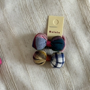 Detail of colorful plaid fabric bow hair ties on a textured linen background with card